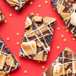 Pieces of s'mores bark on a red background with surrounded by gold star sprinkles