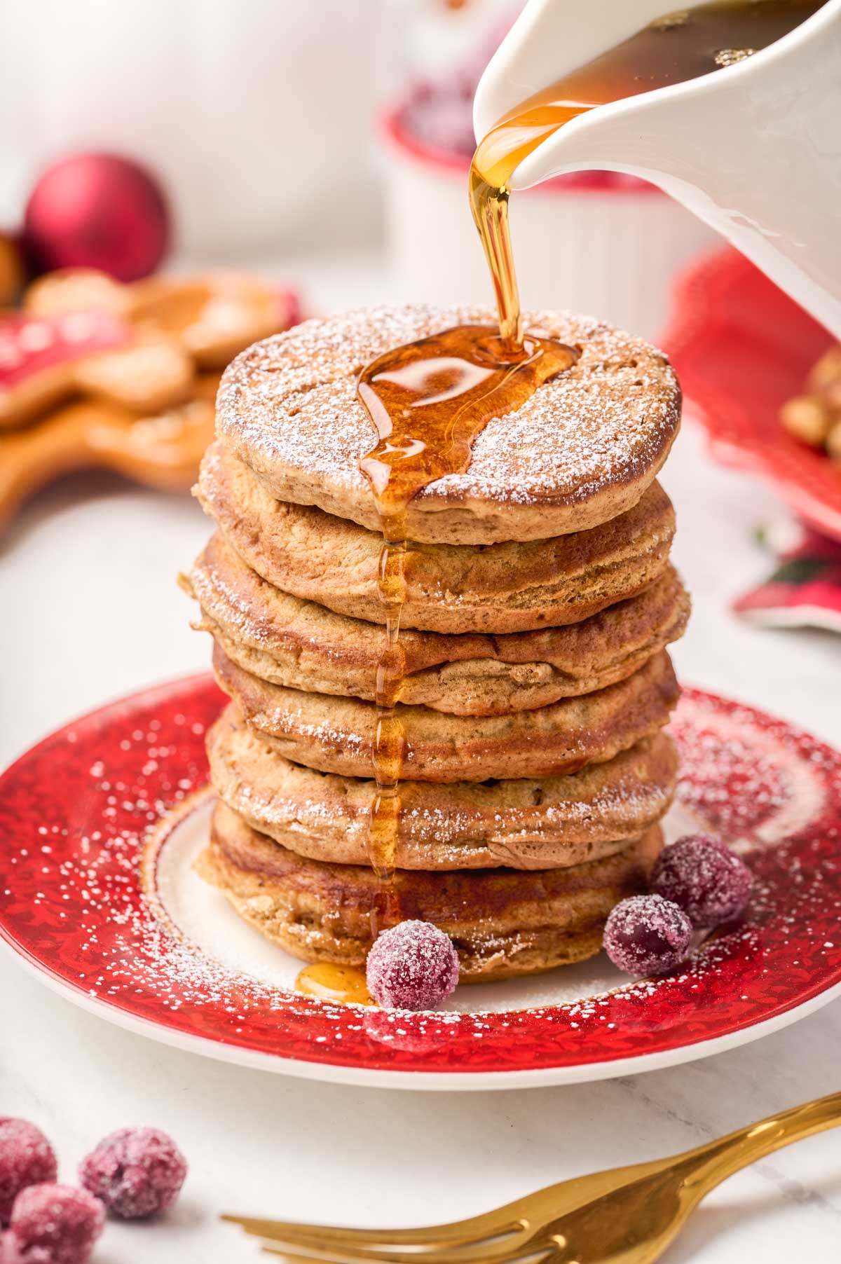 maple syrup being poured over a stack of gingerbread pancakes dusted with powdered sugar