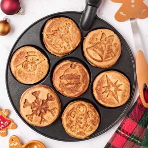 Seven gingerbread pancakes in a pan with holiday designs imprinted on them