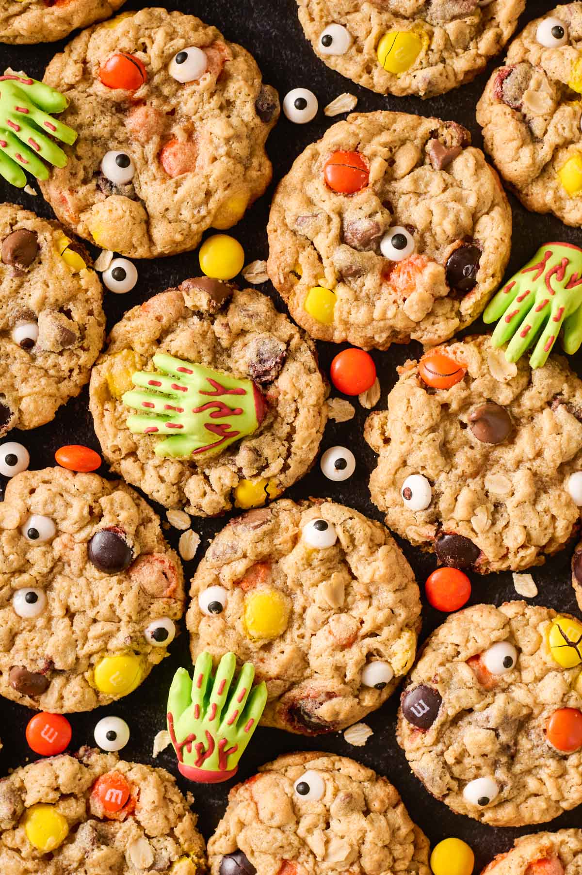 an overhead shot of baked monster cookies on a dark background with decorated with zombie hands, candy eyes and M&Ms
