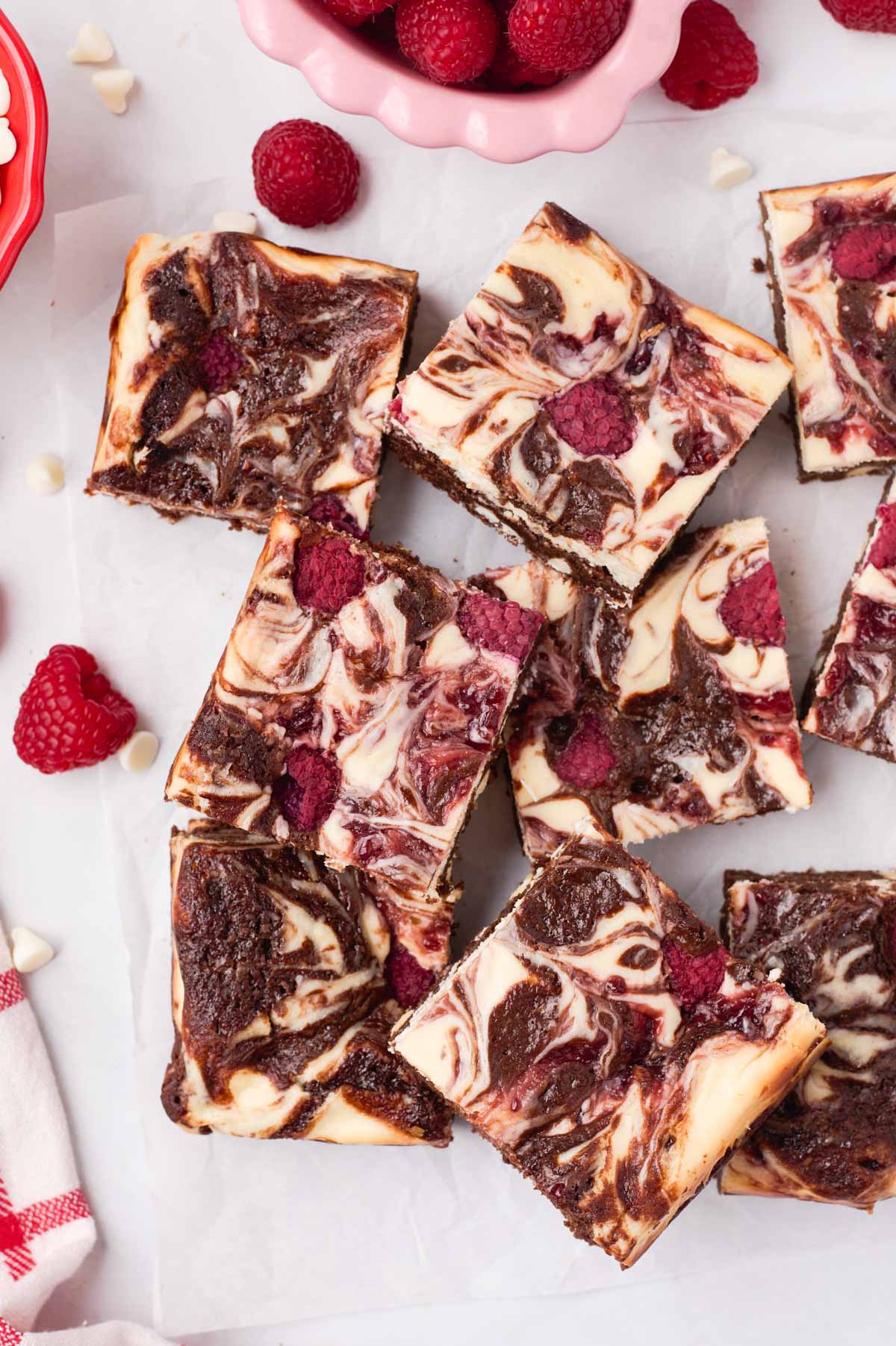 Raspberry cheesecake brownies on parchment paper with fresh raspberries and white chocolate chips
