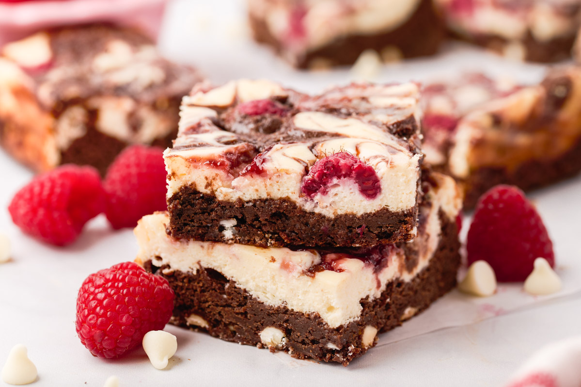 Two raspberry cheesecake brownies stacked with raspberries, white chocolate chips and other brownies surrounding them