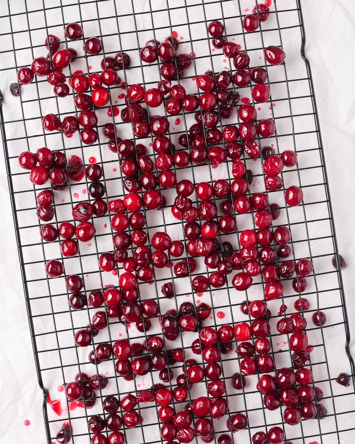 cranberries coated in simple syrup drying on a black wire rack on top of parchment paper