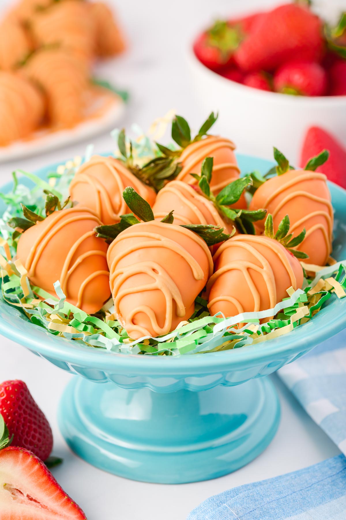 a blue serving dished with decor shreds of grass topped with chocolate covered strawberry carrots
