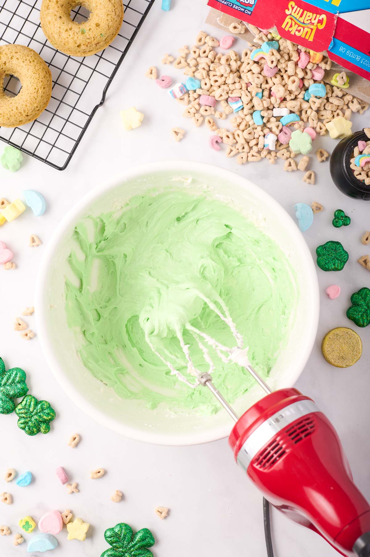 A large mixing bowl with green marshmallow frosting with the red kitchen aid mixer to the side