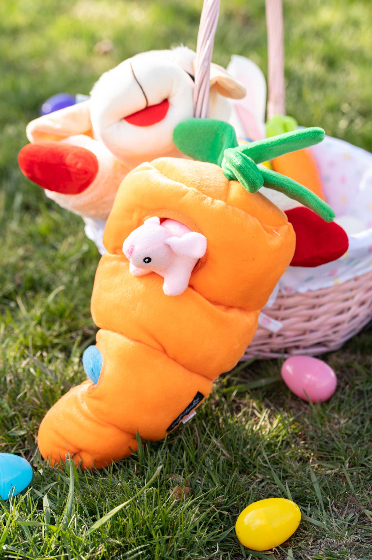A hide and seek toy for dogs in the shape of a large carrot leans against an Easter basket on the grass