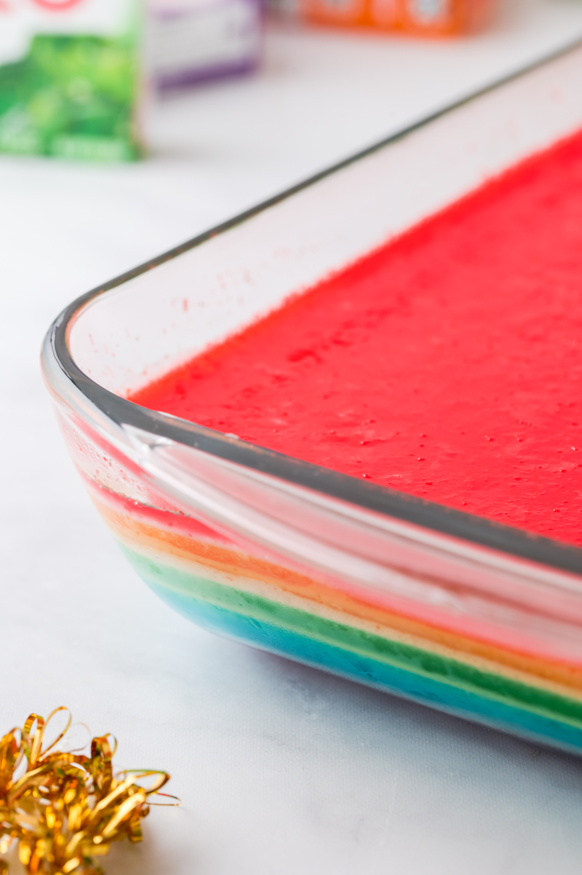 A close up side view of rainbow jello cake in a glass dish to see the layers