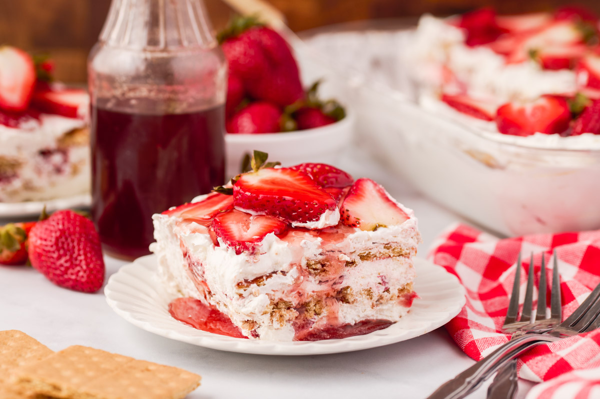 A piece of strawberry icebox cake with strawberry syrup drizzled on top on a white scalloped plate