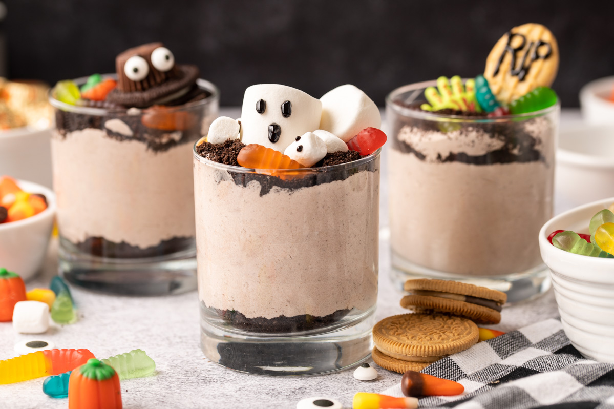 Graveyard dirt cup with marshmallow ghosts and gummy worms surrounded by other dirt cups and candy ingredients