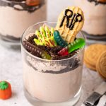 Graveyard dirt cup with a Nutter Butter tombstone, zombie hand and gummy worms surrounded by other dirt cups and candy ingredients