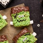 Frankenstein rice kripsie treats sitting on a piece of wax paper on a dark background