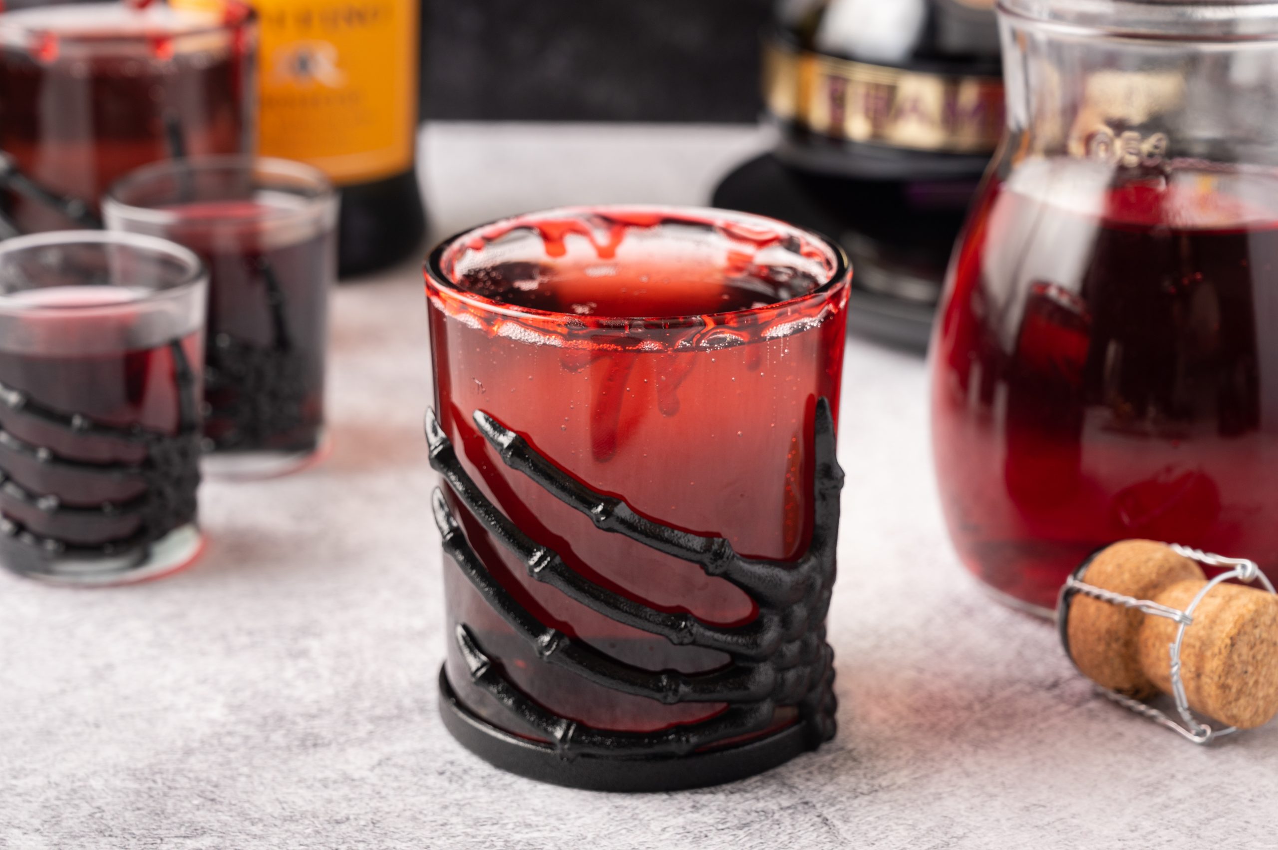 Vampire's Kiss Cocktail served in a glass with a black skeleton hand wrapped around it and the ingredients behind it