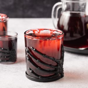 A Vampire's Kiss Cocktail served in glasses with a black skeleton hand wrapped around it