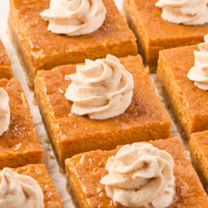 slices of pumpkin pie bars are topped with a swirl of maple spiced whipped cream.