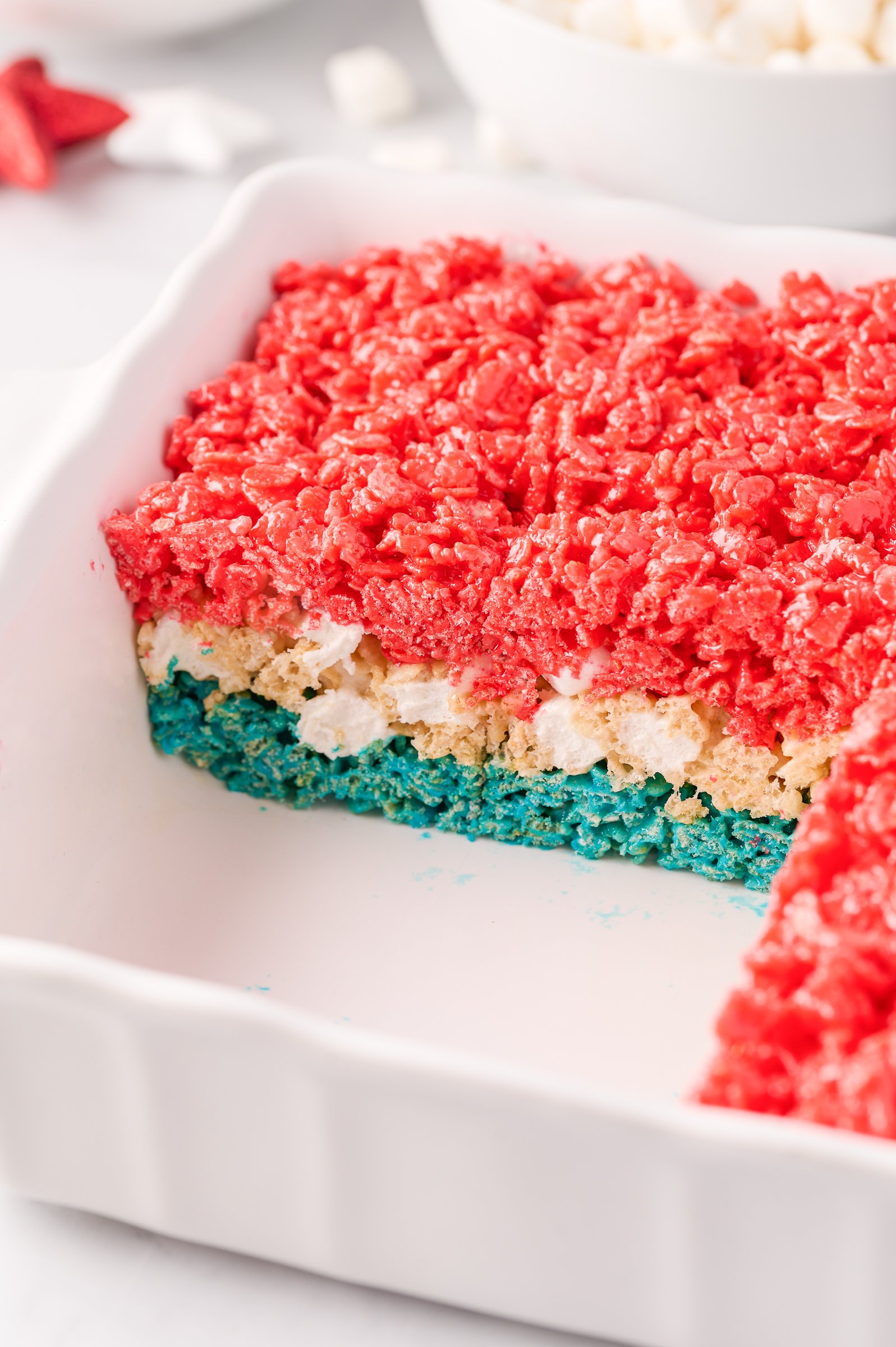 rice krispie treats in a baking dish with a corner of treats removed to reveal the red, white and blue layers of the rice krispie treats