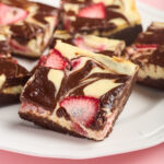 A platter of strawberry cheesecake brownies sits on a pink background.