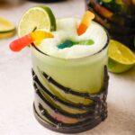 A glass with a black skeleton hand wrapped around it filled with Halloween Lime Sherbet Punch