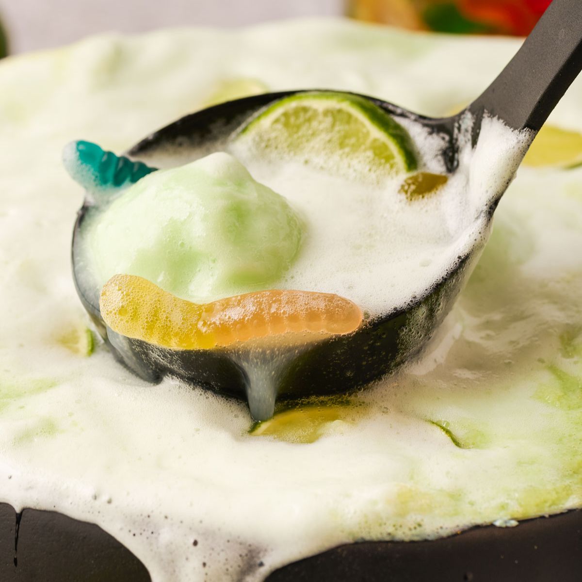 A ladle is scooping Halloween Lime Sherbet Punch out of a cauldron punch bowl